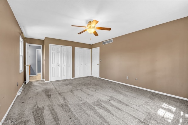 unfurnished bedroom featuring visible vents, carpet floors, baseboards, two closets, and ceiling fan