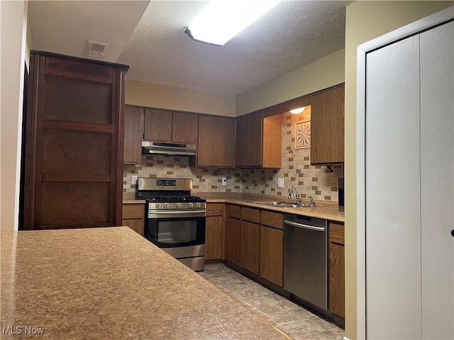 kitchen featuring light countertops, under cabinet range hood, a sink, backsplash, and stainless steel appliances