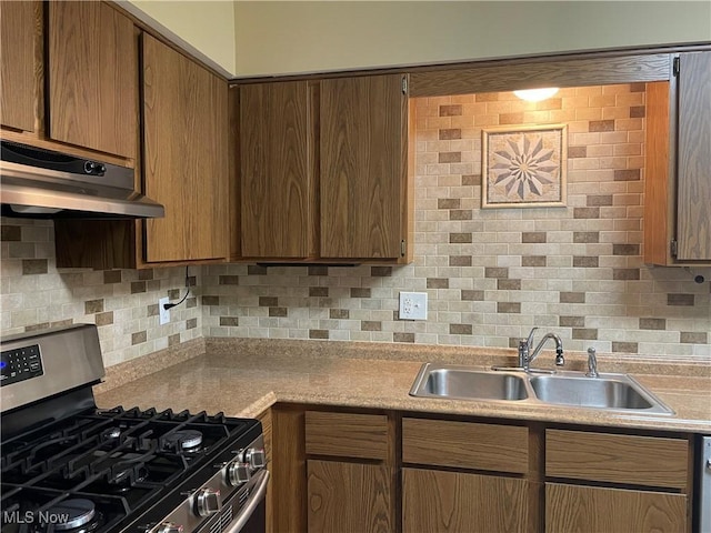 kitchen with under cabinet range hood, backsplash, a sink, and stainless steel gas stove