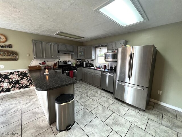 kitchen with stainless steel appliances, a peninsula, a sink, and gray cabinets