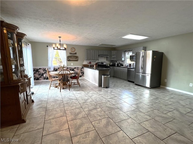 kitchen with dark countertops, a textured ceiling, gray cabinets, an inviting chandelier, and stainless steel appliances