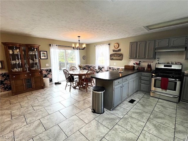 kitchen with dark countertops, gray cabinets, an inviting chandelier, a peninsula, and gas stove