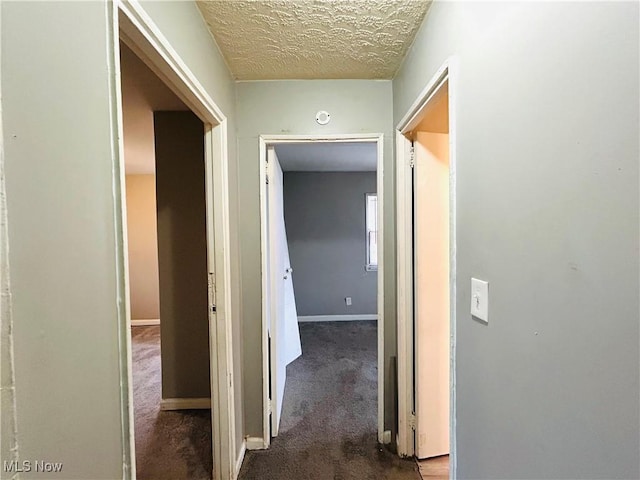 hallway featuring carpet floors, a textured ceiling, and baseboards