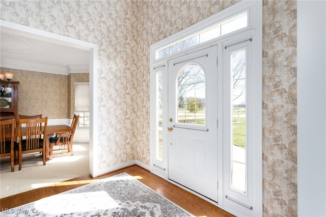 entryway featuring wallpapered walls, baseboards, wood finished floors, and ornamental molding