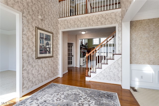 entryway with wainscoting, wallpapered walls, wood finished floors, and stairs