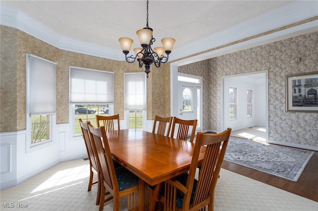 dining space with wallpapered walls, wainscoting, a chandelier, light wood-type flooring, and ornamental molding