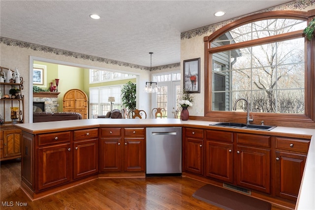 kitchen with stainless steel dishwasher, a sink, a textured ceiling, visible vents, and a fireplace
