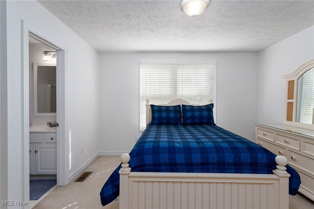 bedroom featuring visible vents, baseboards, a textured ceiling, light colored carpet, and ensuite bathroom