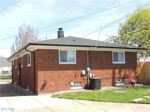 view of side of home featuring central AC unit, a chimney, fence, brick siding, and roof with shingles