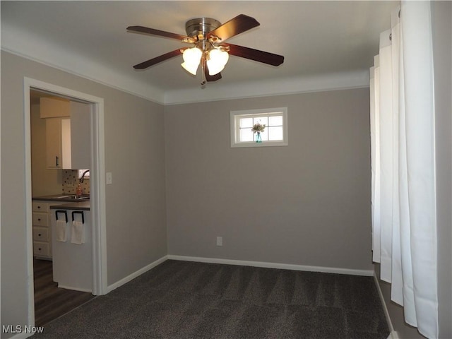 empty room featuring a sink, baseboards, dark carpet, ceiling fan, and crown molding