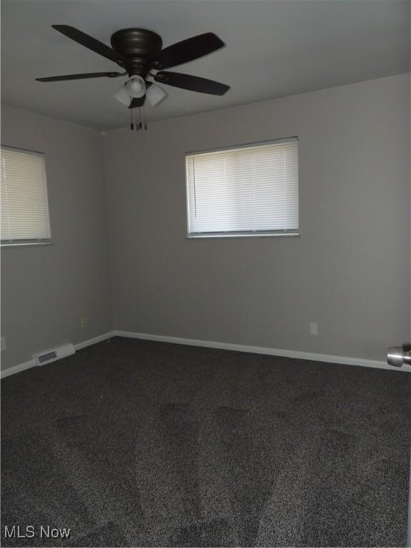 empty room with baseboards, a ceiling fan, dark colored carpet, and visible vents