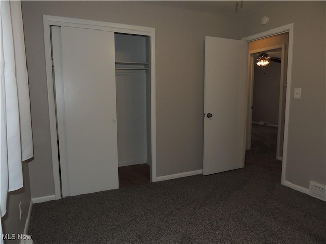 unfurnished bedroom featuring baseboards, dark colored carpet, and a closet