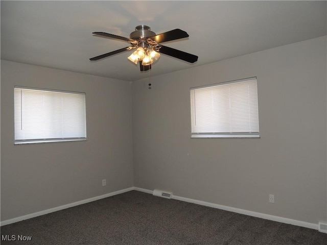 empty room featuring dark carpet, visible vents, baseboards, and ceiling fan