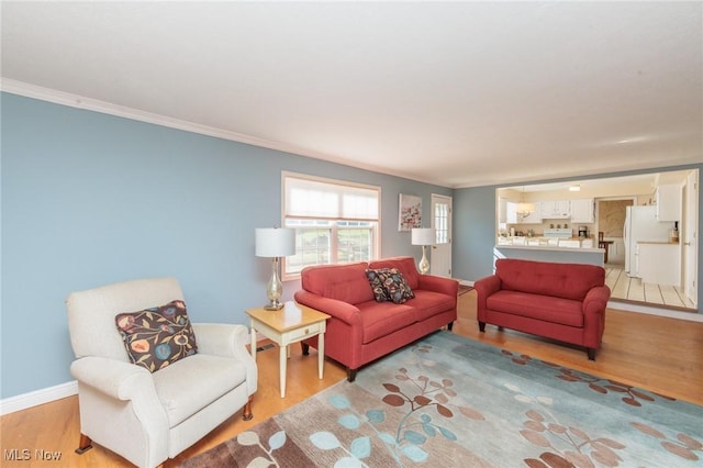 living area with light wood-type flooring, baseboards, and ornamental molding