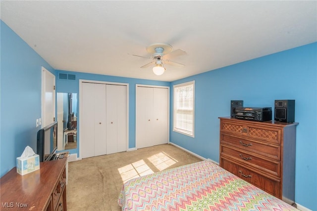 bedroom featuring visible vents, a ceiling fan, light carpet, baseboards, and two closets