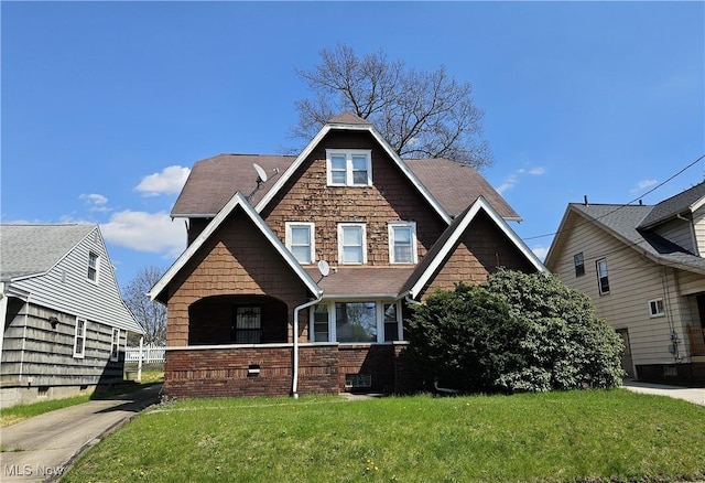 view of front of property featuring brick siding, roof with shingles, and a front yard