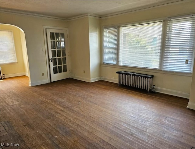 unfurnished room with radiator, arched walkways, crown molding, and wood finished floors