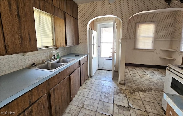 kitchen featuring wallpapered walls, plenty of natural light, a sink, and white appliances