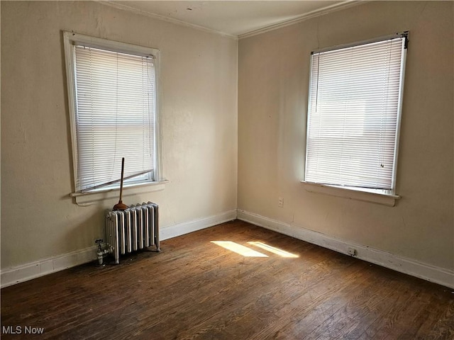 empty room with radiator heating unit, wood finished floors, a wealth of natural light, baseboards, and ornamental molding