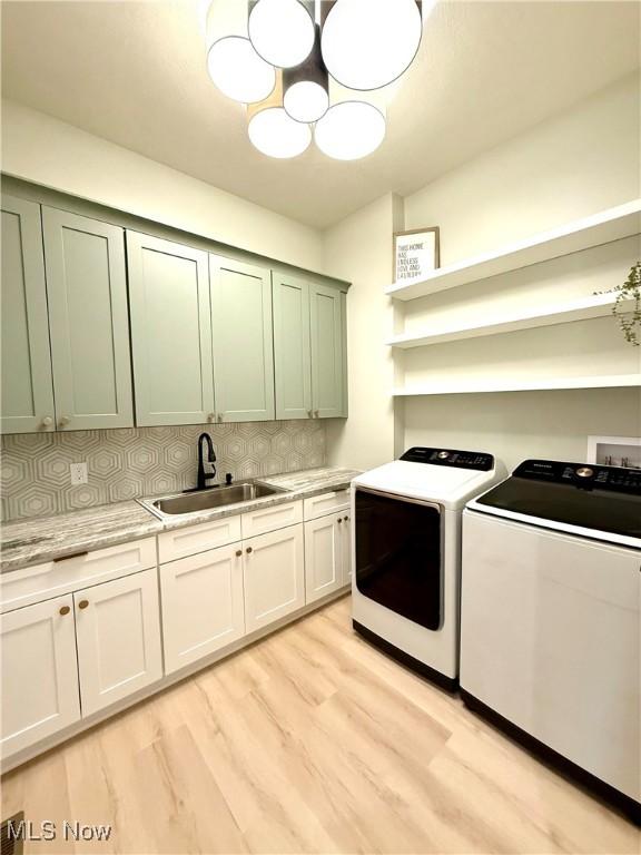washroom with washing machine and dryer, light wood-type flooring, cabinet space, and a sink