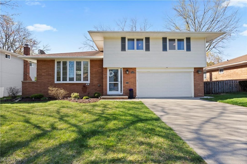 tri-level home featuring concrete driveway, an attached garage, fence, a front yard, and brick siding