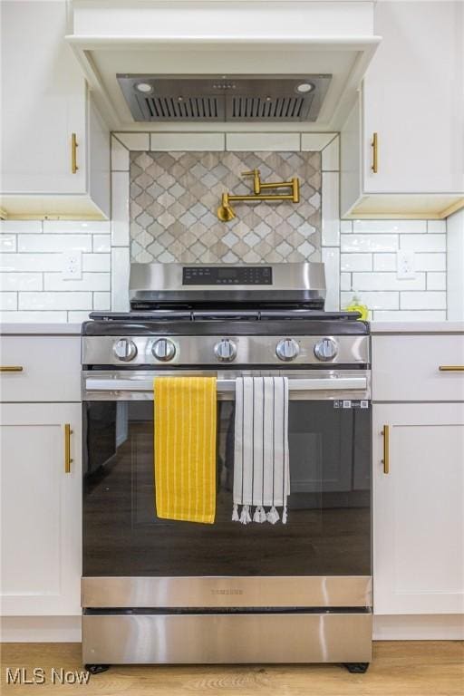 kitchen with wall chimney range hood, stainless steel range with gas stovetop, white cabinetry, and tasteful backsplash