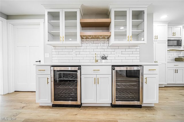 bar with decorative backsplash, wine cooler, built in microwave, and light wood-style flooring