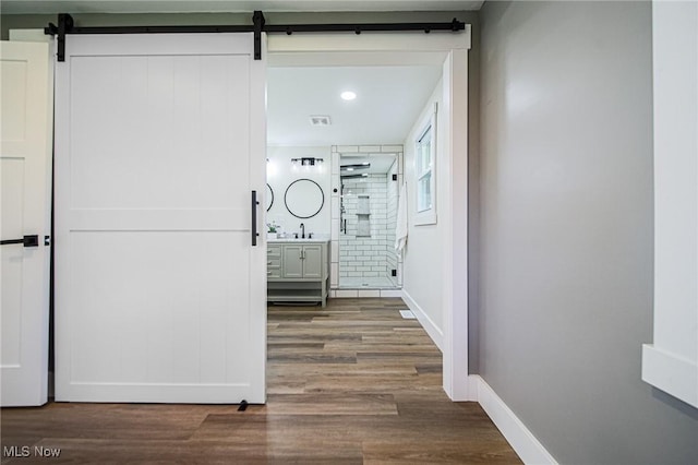 hallway with a barn door, wood finished floors, baseboards, and a sink