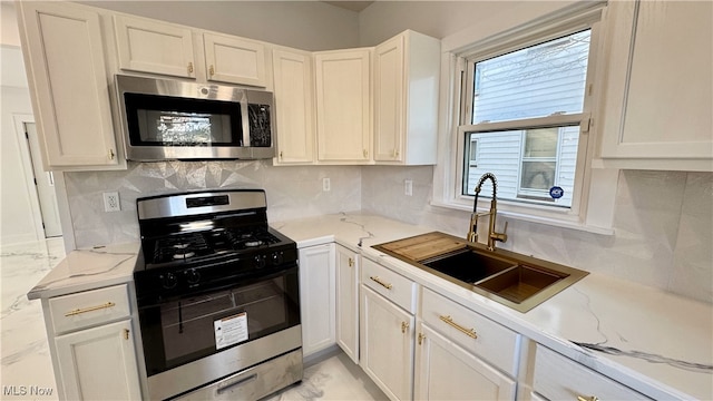 kitchen with backsplash, white cabinetry, stainless steel appliances, and a sink