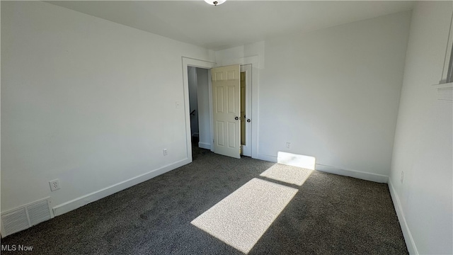 spare room featuring dark colored carpet, visible vents, and baseboards