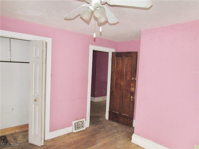 unfurnished bedroom with wood finished floors, visible vents, a closet, baseboards, and ceiling fan