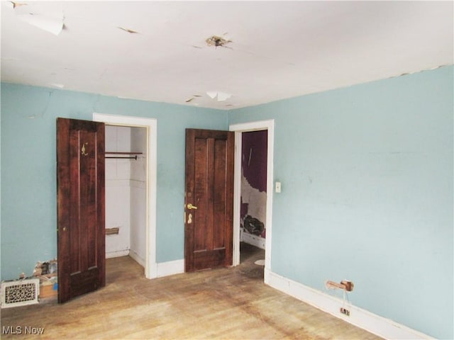 unfurnished bedroom featuring wood finished floors, a closet, a walk in closet, baseboards, and visible vents