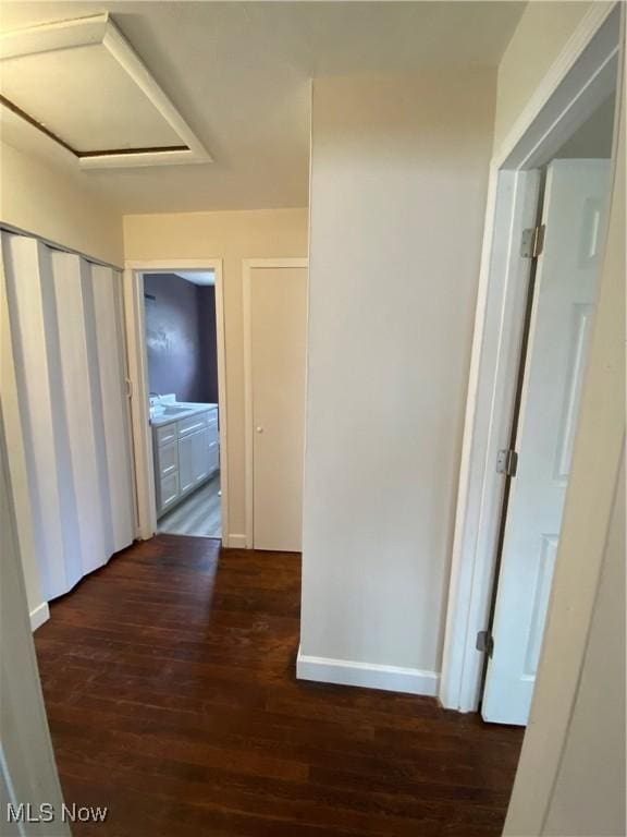 corridor featuring attic access, baseboards, dark wood-style floors, and a sink
