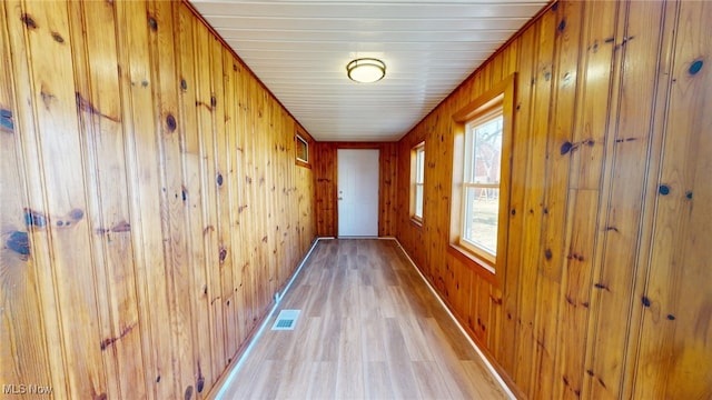 hallway with wooden walls, baseboards, visible vents, and light wood-style flooring
