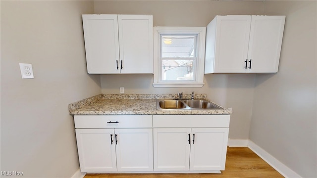 kitchen with a sink, light wood-style floors, light stone countertops, baseboards, and white cabinetry