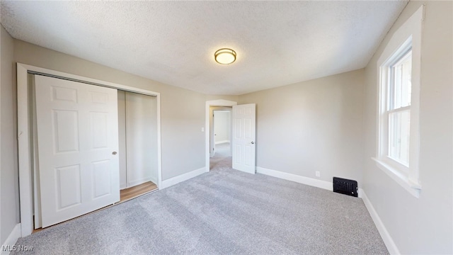 unfurnished bedroom with a textured ceiling, baseboards, carpet floors, and a closet