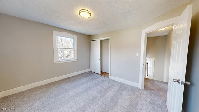 unfurnished bedroom featuring baseboards, a closet, a textured ceiling, and carpet