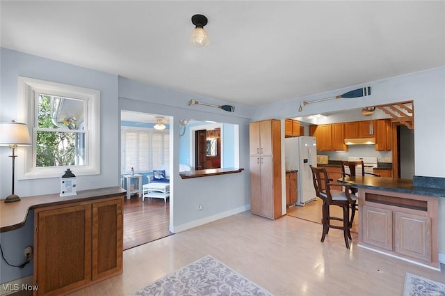 kitchen featuring under cabinet range hood, dark countertops, light wood-style floors, white fridge with ice dispenser, and range