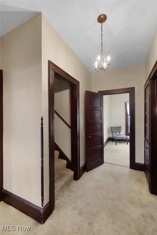 corridor with baseboards, light carpet, stairs, and an inviting chandelier