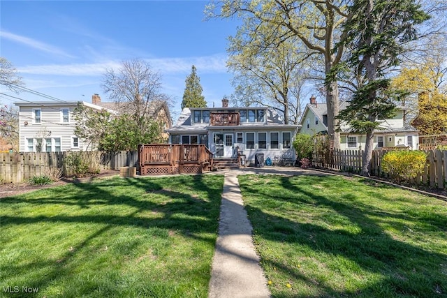 back of house featuring a balcony, a chimney, a fenced backyard, a yard, and a wooden deck