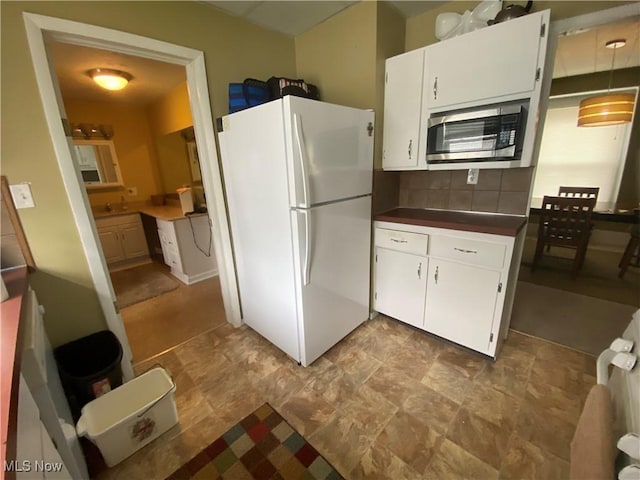 kitchen featuring stainless steel microwave, tasteful backsplash, dark countertops, freestanding refrigerator, and white cabinetry