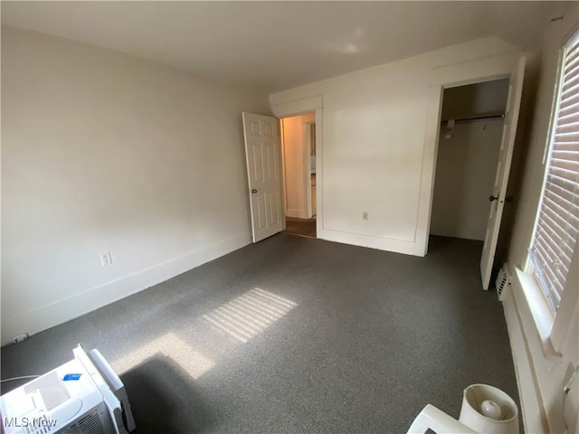 unfurnished bedroom with dark colored carpet, baseboards, and multiple windows