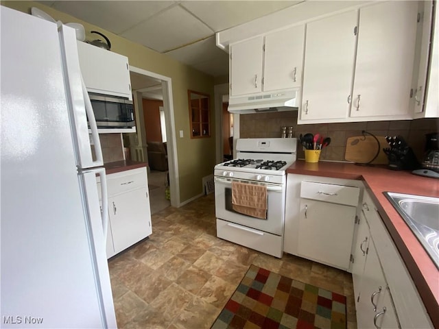 kitchen with white cabinets, backsplash, white appliances, stone finish flooring, and under cabinet range hood