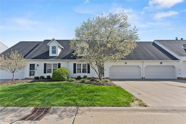 new england style home featuring an attached garage, a shingled roof, a front yard, and driveway