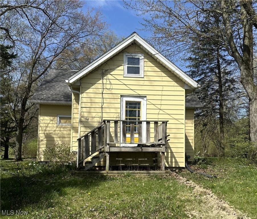 rear view of house with a lawn, a shingled roof, and a deck