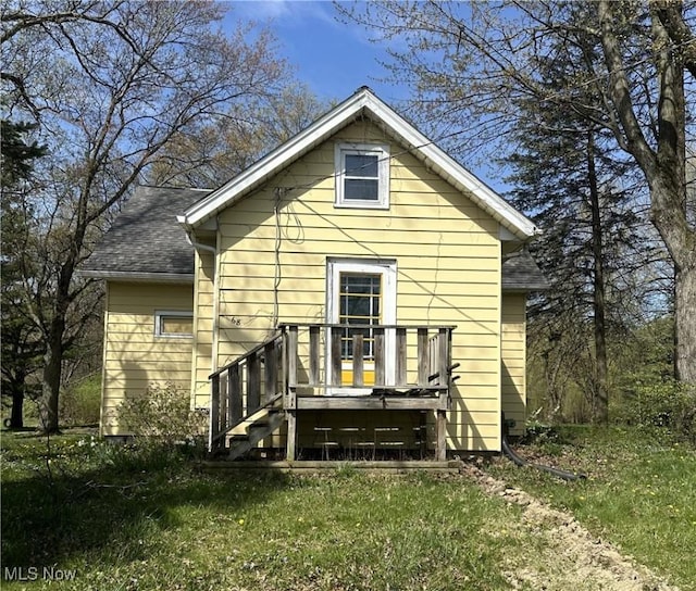 rear view of house with a lawn, a shingled roof, and a deck