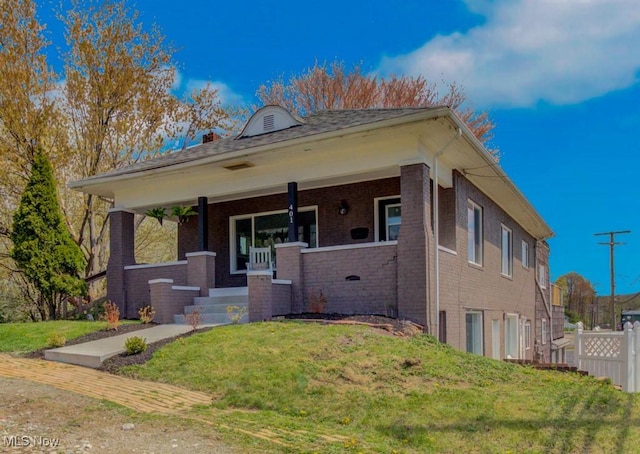 bungalow featuring brick siding, fence, covered porch, and a front yard
