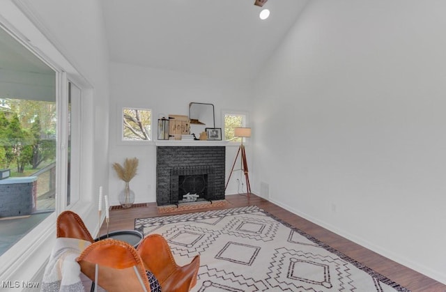 living area with high vaulted ceiling, wood finished floors, a fireplace, baseboards, and visible vents