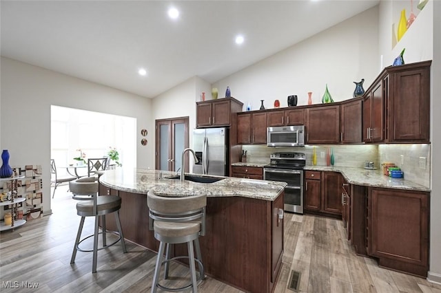kitchen featuring a sink, a center island with sink, lofted ceiling, decorative backsplash, and appliances with stainless steel finishes