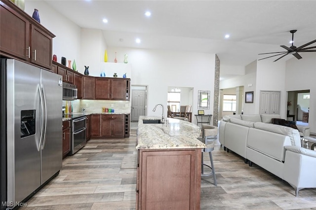 kitchen with high vaulted ceiling, open floor plan, stainless steel appliances, and a sink
